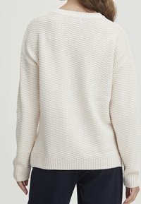 Maglione crema testurizzato con orlo e polsini a coste. Vestibilità rilassata con scollo rotondo, caratterizzato da un delicato motivo geometrico.