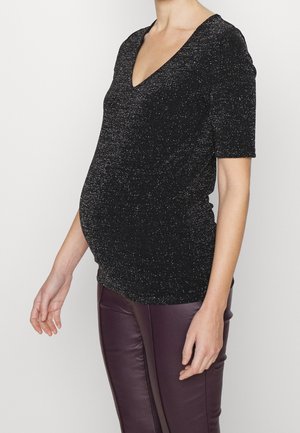 Czarny, krótko rękawowy top z dekoltem w kształcie litery V, o lśniącej fakturze. Nosi się go na dopasowanych ciemnofioletowych spodniach, podkreślając zaokrągloną sylwetkę.