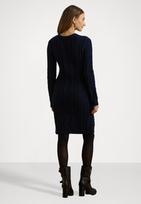 Abito lavorato a maglia blu navy con motivo a trecce, maniche lunghe e orlo a coste. Abbinato a stivali neri al ginocchio con tacco.