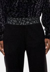 Pantaloni neri con un tessuto testurizzato, caratterizzati da una vita grigio scuro adornata con un sottile motivo astratto.
