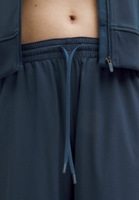 Mornarsko sportske kratke hlače s elastičnim pojasom i vezicom, izrađene od glatkog, laganog materijala, uz dodatak detalja s patentnim zatvaračem na jakni.