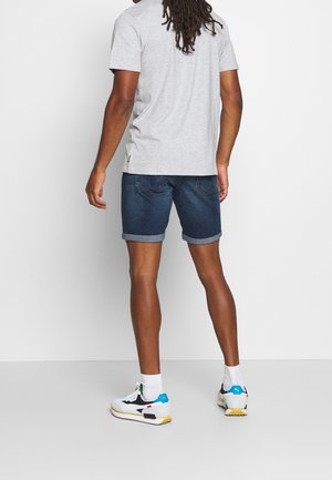 T-shirt grigio a maniche corte, pantaloni corti di denim con risvolti e scarpe da ginnastica multicolori, viste di spalle su uno sfondo neutro.