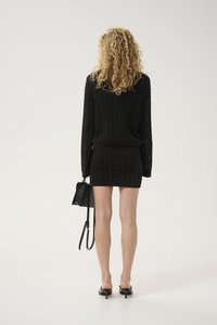 Black knitted sweater dress with a ribbed texture, long sleeves, and a fitted silhouette, paired with a small black handbag.