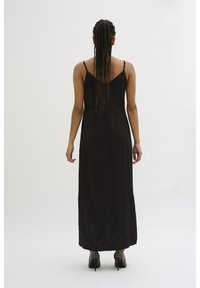 Robe maxi noire sans manches avec une texture lisse, dotée de fines bretelles et d'un design fluide. Associée à des chaussures à talons scintillantes.