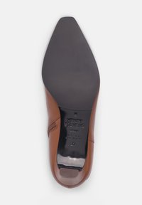 Chaussure en cuir marron avec un embout pointu, texture lisse et semelle noire. Présente un marquage sur la semelle intérieure et un design de talon arrondi.