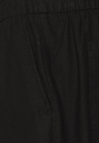 Pantaloni in lino neri con elastico in vita, dotati di tasche laterali, superficie testurizzata e design semplice.