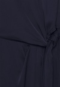 Tecido azul marinho com detalhe em nó na cintura, com uma textura suave e um design fluido. Costura mínima é visível.