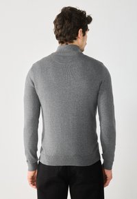 Pull en tricot gris avec un col montant, design ajusté, manches longues et ourlet côtelé. Le matériau semble doux et texturé. Vue de dos montrée.