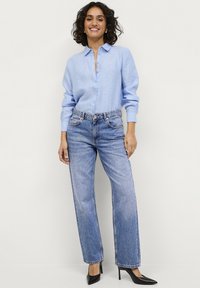 Camisa de botones celeste, con cuello y mangas largas, combinada con unos vaqueros de tiro alto en azul desgastado y tacones negros de punta.
