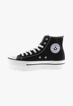 Sneaker alta nera in tela, con punta bianca e lacci bianchi, un'etichetta rotonda con logo e una suola piatta bianca a strati.