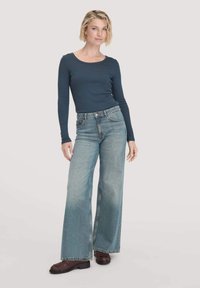 Een donkerblauwe top met lange mouwen gecombineerd met lichtblauwe jeans met een brede broekspijp. De jeans hebben een vervaagde afwerking, vijf zakken en zichtbare stikseldetails.