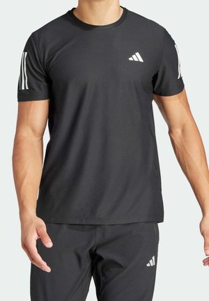 Homme portant un T-shirt Adidas noir à manches courtes et un short noir avec des logos Adidas blancs sur la poitrine, les manches et la cuisse.