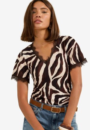 Vrouw draagt een top met zebraprint en kanten rand rond de hals en mouwen, gecombineerd met een blauwe spijkerbroek en een bruine riem.
