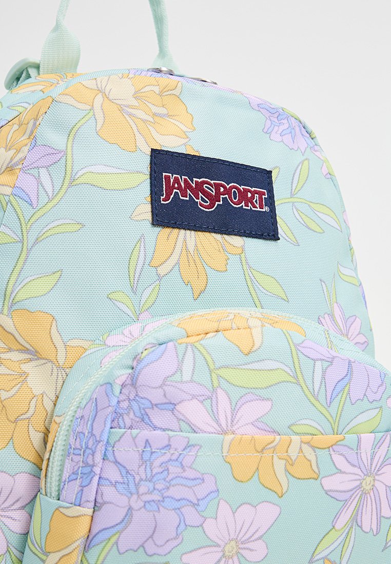 Zaino floreale azzurro chiaro con fiori gialli e viola; presenta una tasca anteriore e un'etichetta con il logo JanSport su uno sfondo scuro.