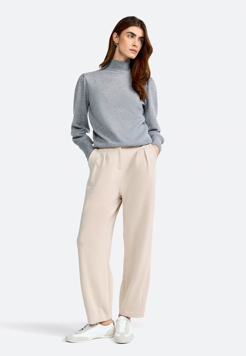 Lichtgrijze trui met hoge nek, gecombineerd met beige hoge taille broek en witte sneakers. Glad materiaal en een relaxte pasvorm.