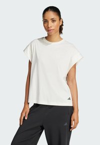 Witte korte mouwen sport T-shirt met een ontspannen pasvorm, een soepele textuur en een klein zwart logo op de linker onderzoom, gedragen met donkere broek.