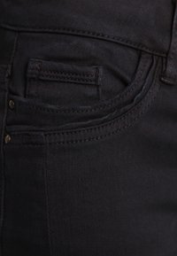 Zwarte denim jeans hebben een voorzak met subtiele stikdetails en een metalen knop, en tonen een gladde textuur en een op maat gemaakt ontwerp.