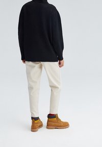 Czarny sweter dzianinowy z wysokim kołnierzem, w połączeniu z kremowymi spodniami i brązowymi butami na sznurowadłach z żółtymi akcentami i szarymi kołnierzami.