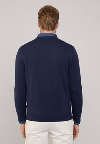 Maglione lavorato a maglia blu navy, collo rotondo, maniche lunghe, con polsini e orlo a coste, abbinato a una camicia blu con colletto sotto.