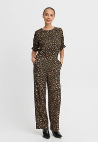 Combinaison à imprimé léopard en noir et beige, dotée de manches courtes, d'une coupe décontractée, de poches latérales et de jambes larges à longueur de cheville.