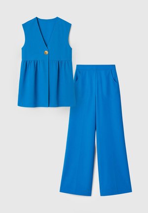 Blaues ärmelloses V-Ausschnitt-Top mit Knöpfen, kombiniert mit weit geschnittenen Hosen mit Seitentaschen, vor weißem Hintergrund dargestellt.