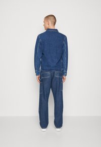 Giubbotto in denim blu scuro con colletto, abbinato a jeans a gamba larga con tasche applicate. Texture liscia e dettagli di cuciture a contrasto.