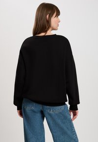 Czarna, oversize bluza z okrągłym dekoltem i teksturowanym materiałem, zestawiona z jasnoniebieskimi spodniami dzwonami z tylnymi kieszeniami.