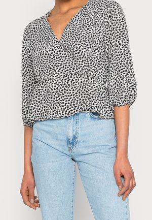 Blusa a fantasia bianco e nero con scollatura a V, maniche a tre quarti e taglio morbido, abbinata a jeans azzurri a vita alta.
