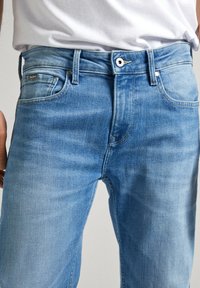 Vaqueros de denim azul claro con un corte recto, diseño de cinco bolsillos y cierre de botón, con un ligero desgaste y un logotipo bordado en el bolsillo trasero.