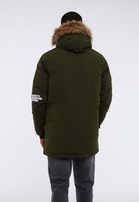 Long olive green puffer jacket with faux fur trim on the hood. Features black accents and white branding on the right sleeve.