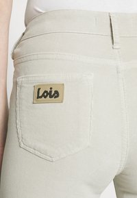 Beige kordfloddsbyxor med en liten rektangulär Lois-logotyp på bakfickan. Sömmarna är synliga längs med sömmarna.