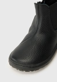 Black leather ankle boot with textured finish, rounded toe, and side zipper closure; flexible black sole and elastic side panels.