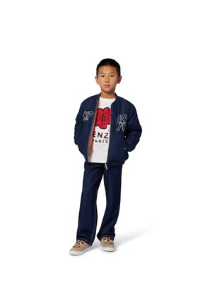 Denim bomberjack met geborduurde details, witte graphic T-shirt met rode bloem, donkere jeans en tan sneakers met decoratieve accenten.