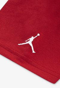 Punainen kangas, jossa on sileä pinta, sisältää valkoisen Jumpman-logon, joka esittää siluettia henkilöstä hyppäämässä koripallon kanssa.