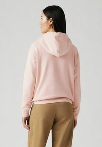 Pink hoodie with a relaxed fit, featuring a drawstring hood, ribbed cuffs, and hem. The material appears soft with a smooth texture.