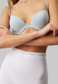 Reggiseno imbottito azzurro chiaro con spalline regolabili e finitura liscia, abbinato a mutandine bianche a vita alta con cintura logata Calvin Klein.