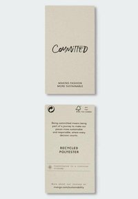 Etikett med beige bakgrunn, med svart tekst som leser "Forpliktet" og tilleggsinformasjon om bærekraft knyttet til resirkulert polyester.