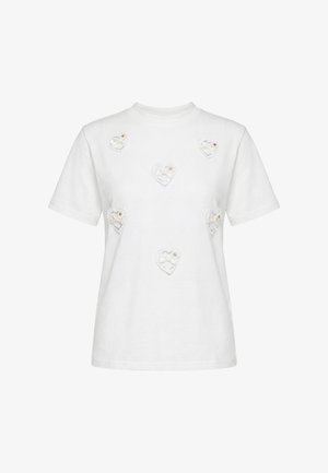 T-shirt blanc à manches courtes avec six petits patchs en dentelle en forme de cœur, chacun avec un nœud et un petit détail fleuri sur le devant.
