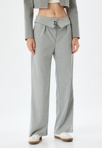 Pantalones de pierna ancha de color gris claro, hechos de una tela suave, con una cinturilla doblada, dos botones y un diseño minimalista.
