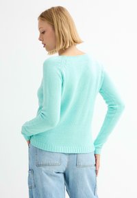 Suéter de punto verde menta con mangas largas, dobladillo acanalado y escote redondo. La textura es suave con un sutil detalle en los hombros.
