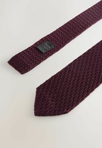 Cravatta tessuta bordeaux con un motivo testurizzato, caratterizzata da un'estremità stretta e un'etichetta attaccata all'estremità più larga.