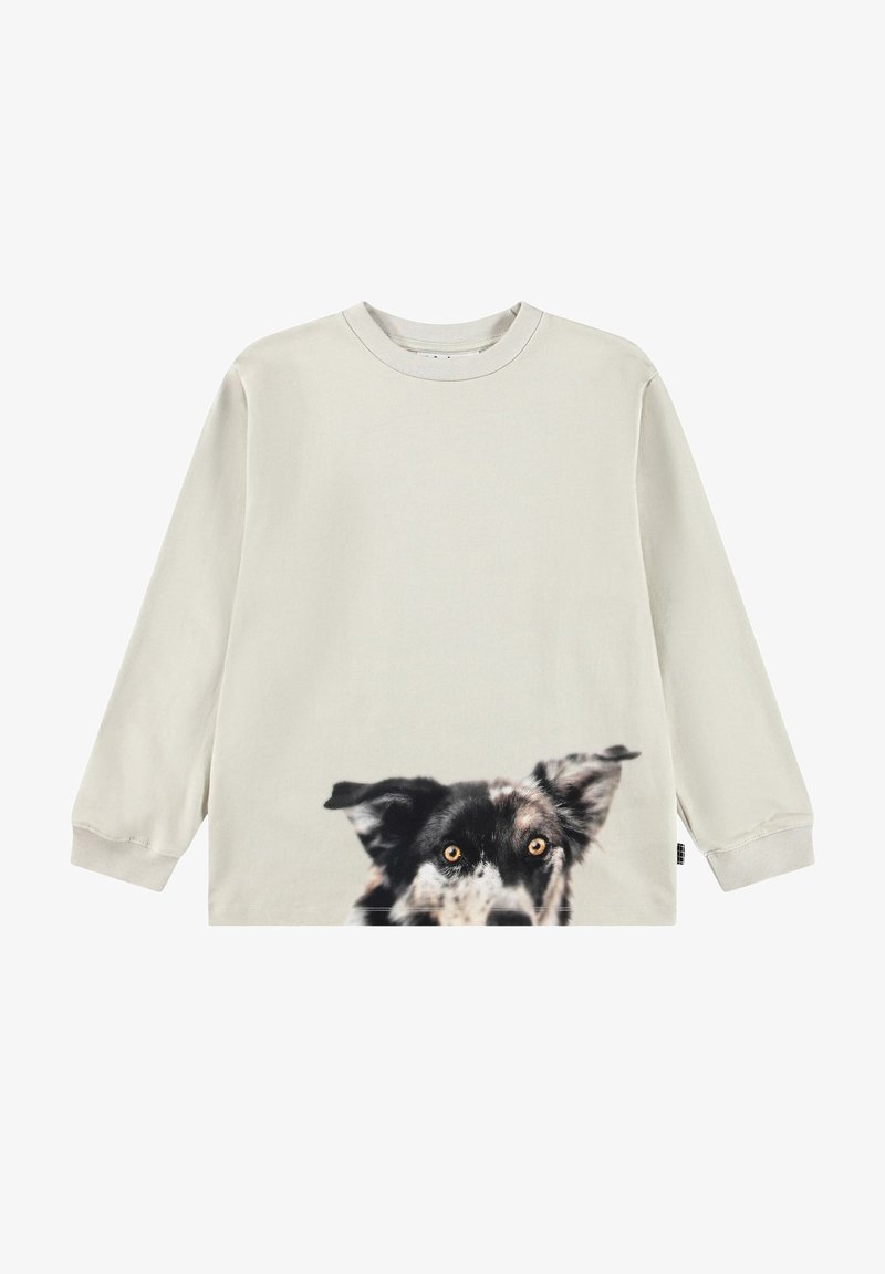 Chemise beige à manches longues présentant la partie supérieure du visage d’un chien noir et blanc aux yeux ambrés imprimée près de l’ourlet.