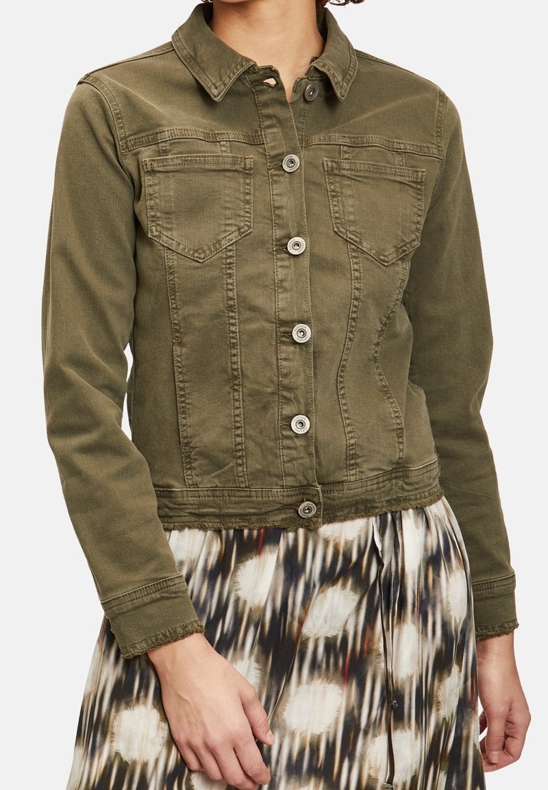 Chaqueta vaquera de color verde oliva con cuello de solapa, cierre de botones, dos bolsillos en el pecho y diseño ajustado. Bajo deshilachado y tejido texturizado visibles.