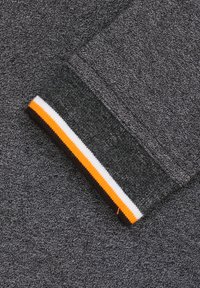 Donkergrijze sweatshirtstof met een gestructureerd oppervlak. De manchette heeft een gestreept patroon in wit, oranje en donkerbruin.