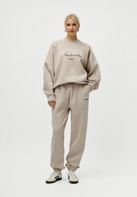 Beige hettegenser med teksten "MODERN Neutrality" og matchende joggebukser. Myk kvalitet, avslappet passform, ribbestrikkede mansjetter og elastisk midjebånd.