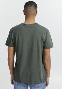 Mørkegrønn t-skjorte med kort erm og avslappet passform, rund hals og myk tekstur, kombinert med lyseblå jeans i midjen.