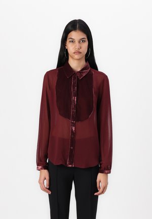 Burgundy sheer button-up shirt with a velvet collar and front panel. Features long sleeves and a relaxed fit, complemented by a subtle sheen.