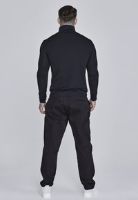 Black turtleneck top and black cargo pants, featuring pockets, worn with white sneakers. Smooth texture, fitted design in a neutral color palette.