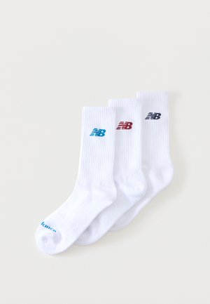 Trois paires de chaussettes blanches montantes avec des logos New Balance bleus, rouges et noirs, disposées côte à côte sur un fond blanc.
