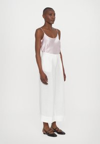 Satin pink camisolilla con tirantes finos combinada con pantalones de lino blancos de corte holgado y zapatos planos negros con tirantes y detalles dorados.